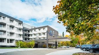 Moderne Best Western Hotel-Fassade mit Balkonen, großem Logo, überdachtem Eingang und geparkten Autos bei teils bewölktem Himmel.