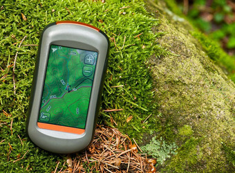 Hand-GPS auf moosbedecktem Felsen, zeigt topografische Karte mit Höhenlinien, Wegpunkten und Navigationssymbolen.