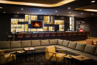 Moderne Lounge mit großer Sofaecke, Sesseln und Couchtisch, im Hintergrund beleuchtete Bar mit Flaschen und Gläsern.