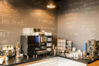 Cafétheke mit Kaffeemaschine, Bechern, Zubehör und Sprüchen an der Wand in Kreideschrift.