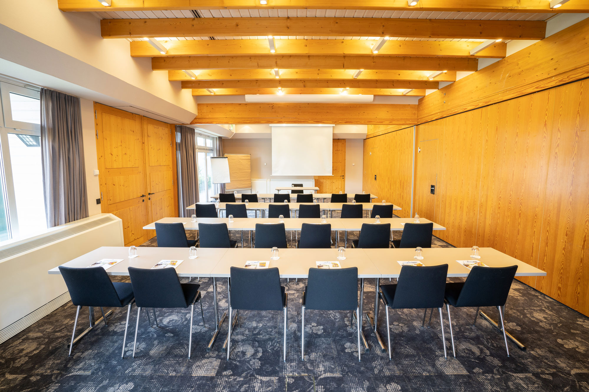 Moderner Konferenzraum mit langem Tisch, schwarzen Stühlen, Holzverkleidung und großen Fenstern für Tageslicht.