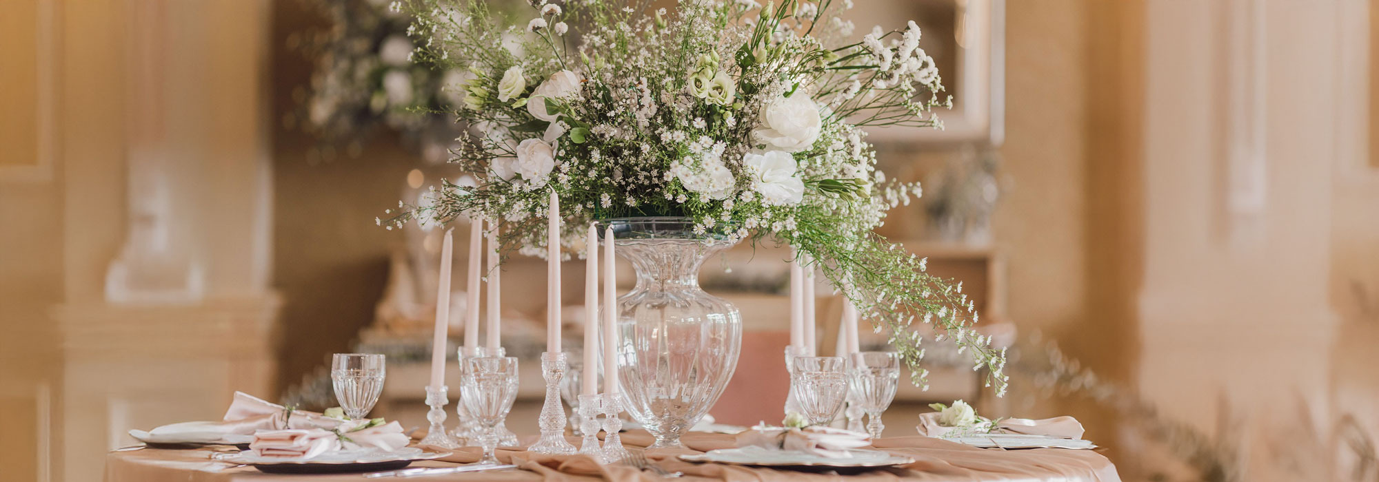 Festlich gedeckter Tisch mit Blumenarrangement, Kristallgläsern, weißen Kerzen und ordentlich gefalteten Servietten.